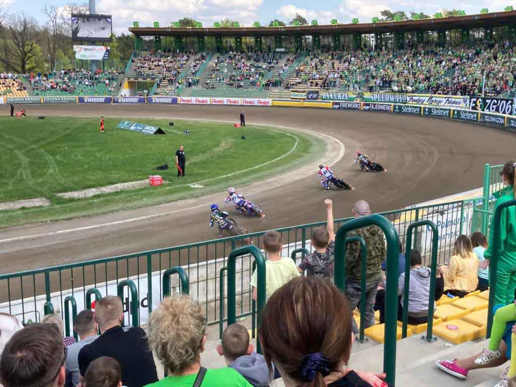 Ludzie na trybunach, tor żużlowy, cztery osoby na motocyklach