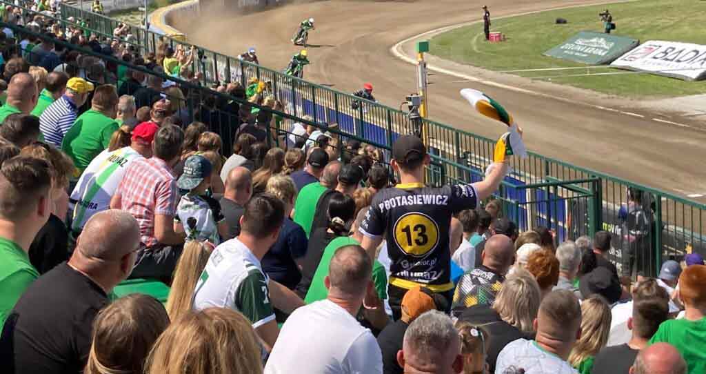 Kibice na trybunach i cztery osoby ścigające się na motocyklach