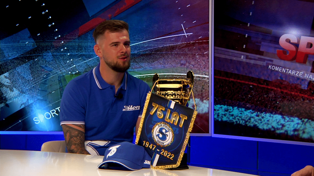 Młody mężczyzna, przed nim puchar, proporczyk i czapeczka