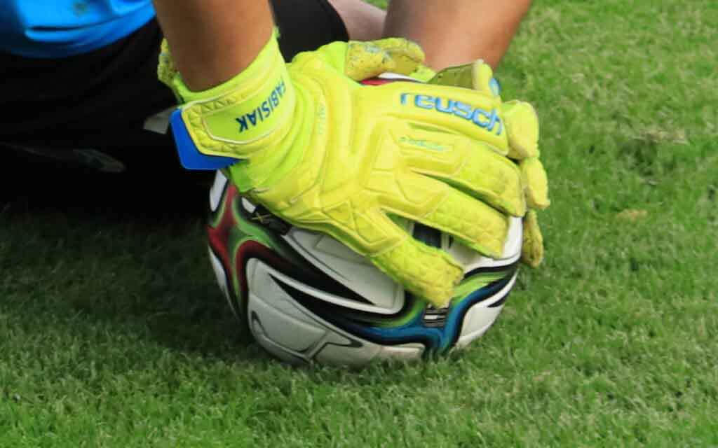 Piłka nakryta dłońmi w rękawicach bramkarskich