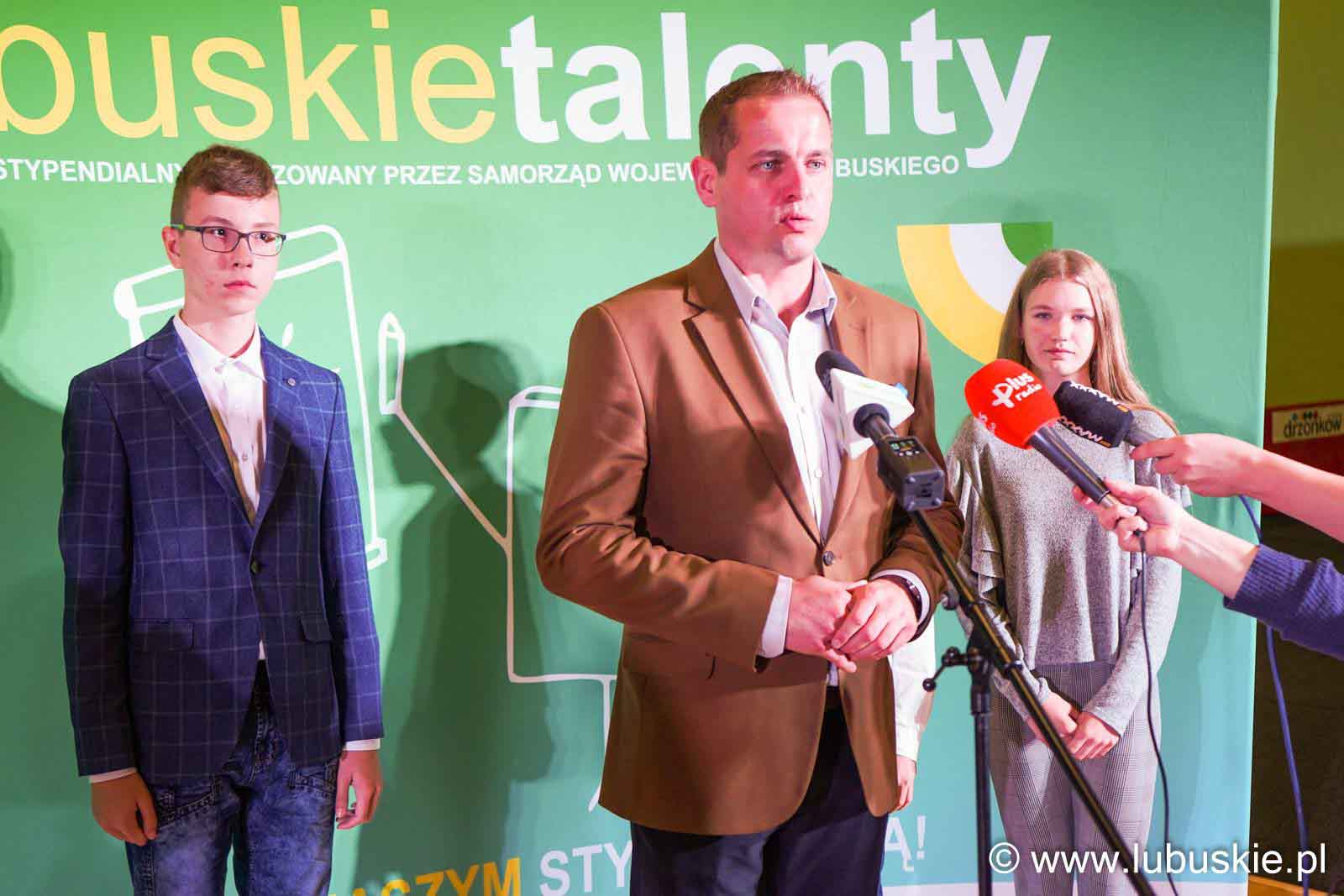 Mężczyzna i dwie młode osoby na tle zielonej planszy  Prawie 700 stypendiów dla najzdolniejszych uczniów w II etapie programu Lubuskie Talenty WIDEO