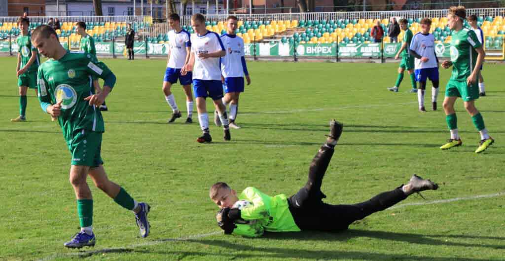 Jedenastu chłopców na boisku. Jeden trzyma piłkę