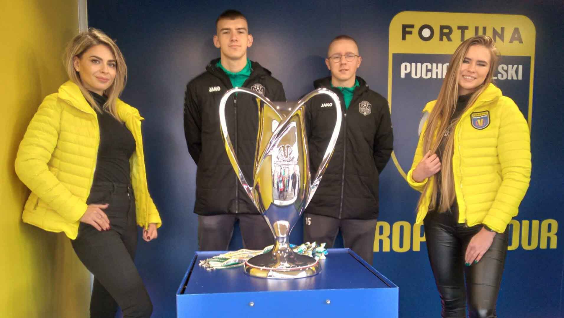 Dwie kobiety i dwaj mężczyźni przy okazałym pucharze  Rezerwujcie termin 28 lutego Lechia Zielona Góra zagra z Legią Warszawa