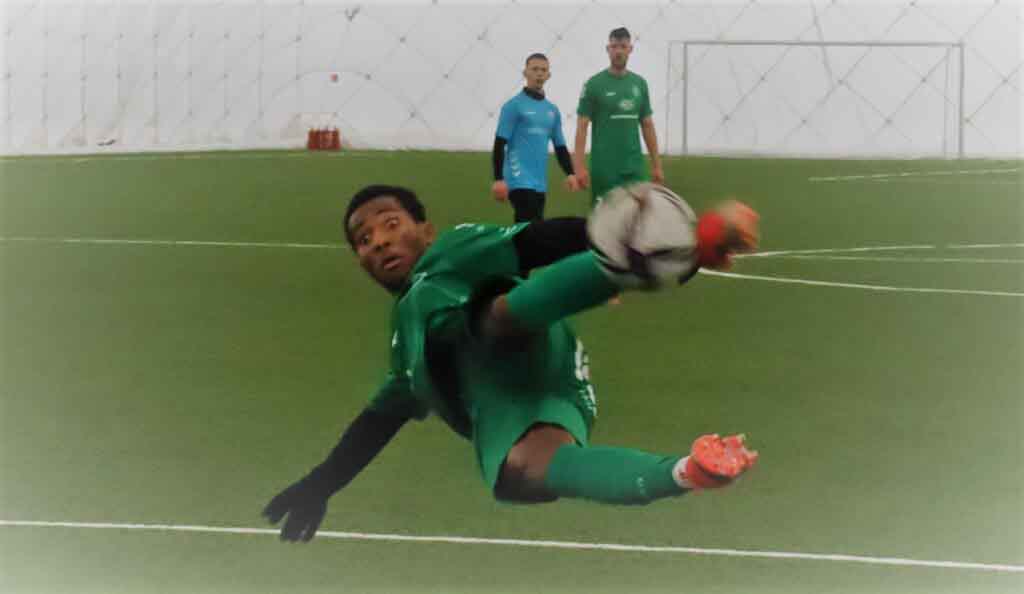 Mężczyzna w ekwilibrystycznej pozycji kopiący piłkę