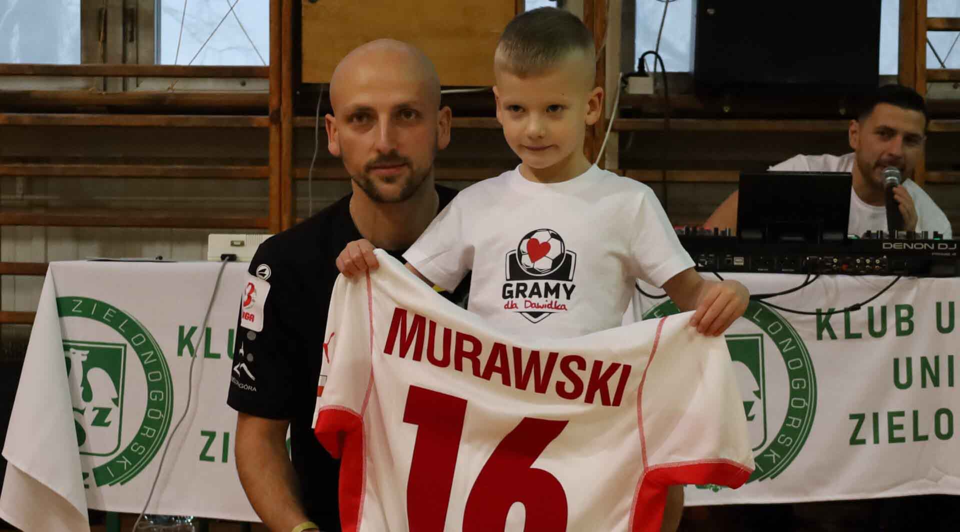 Mężczyzna z dzieckiem prezentującym sportową koszulkę  Turniej Gramy dla Dawidka w Zielonej Górze W akcji Protasiewicz Dudek Drozdowicz ZDJĘCIA