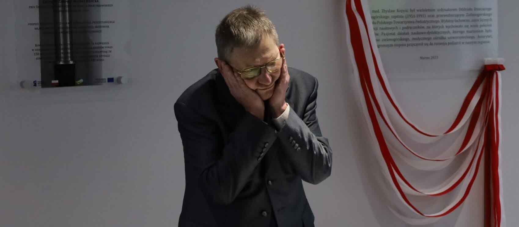 Mężczyzna w garniturze trzymający się obiema dłońmi za głowę  Centrum Zdrowia Matki i Dziecka ma patrona Kim był Zbysław Kopyść WIDEO