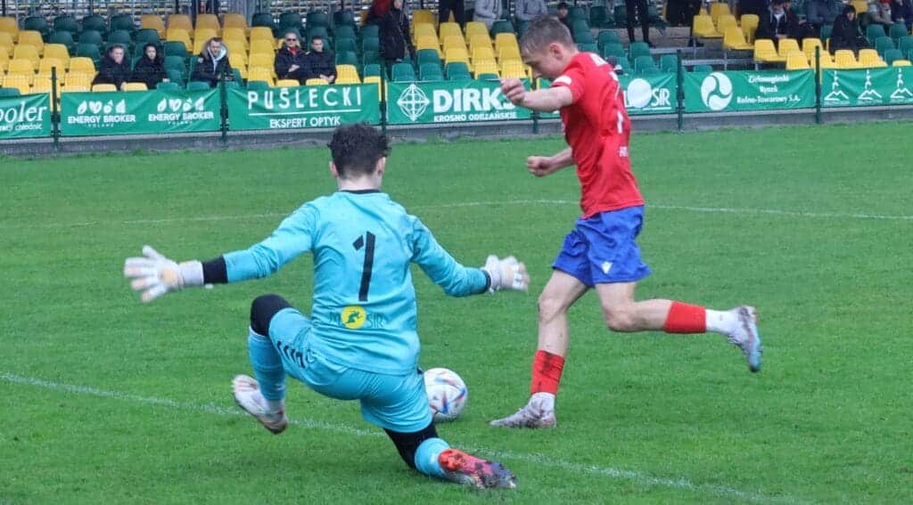 Dwóch chłopców na piłkarskim boisku. Jeden strzela, drugi broni