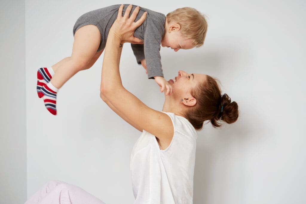 Young mother with her one years old little son dressed in pajamas are relaxing and playing in the bedroom at the weekend together, lazy morning, warm and cozy scene. Selective focus.