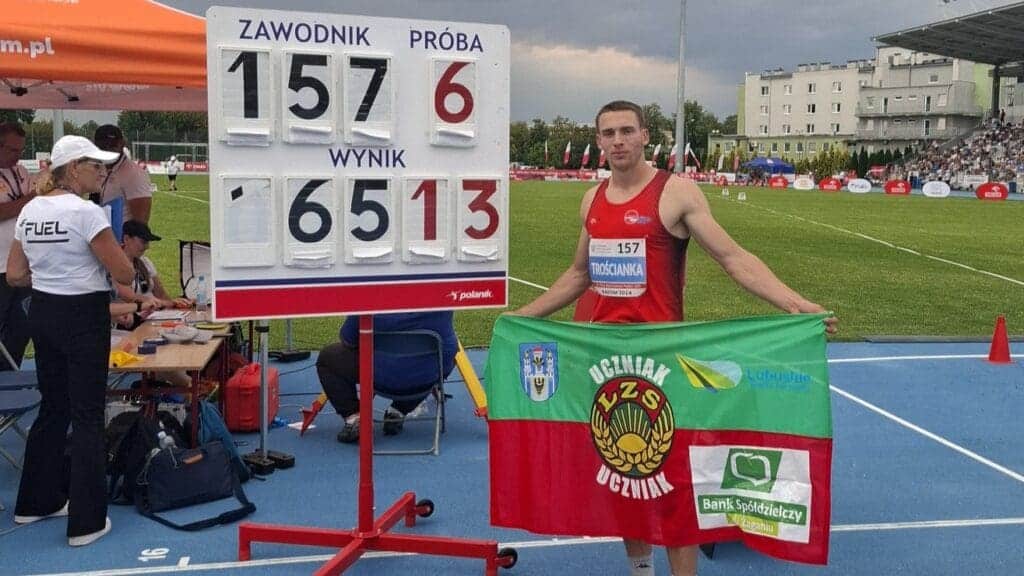 Młody sportowiec pozujący z flagą przy tablicy wyników