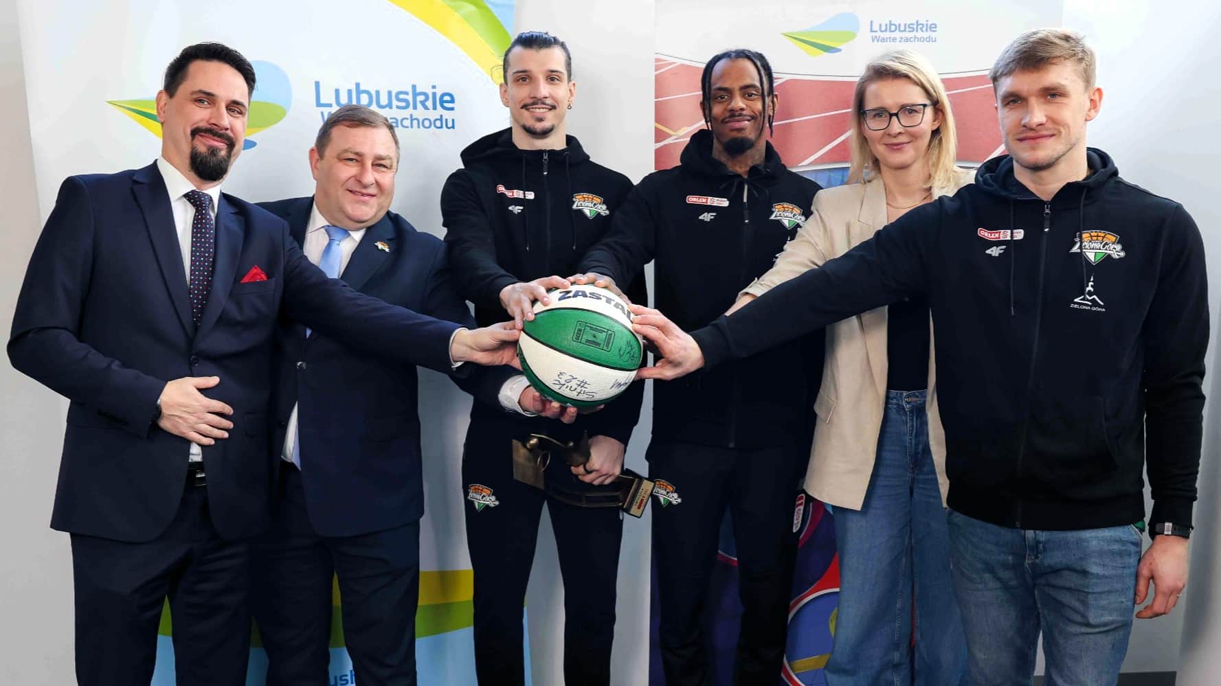 Sześć uśmiechniętych osób z dłońmi na piłce do koszykówki  Pół miliona złotych dla Zastalu od samorządu województwa WIDEO