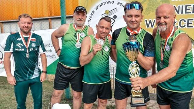 Pięciu mężczyzn w sportowych strojach, z medalami i pucharem