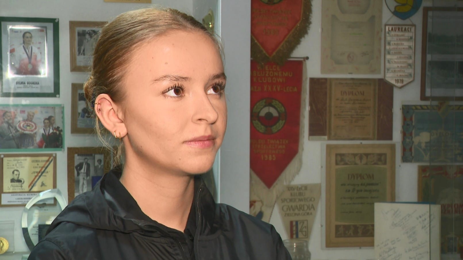 Kobieta na tle dyplomów i proporczyków  Medale strzelców Gwardii i Kadeta na mistrzostwach Polski