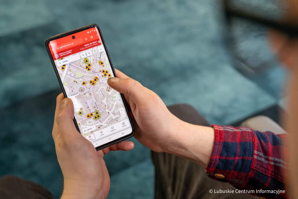 Na zdjęciu osoba trzyma telefon z otwartą aplikacją "Gdzie się ukryć"