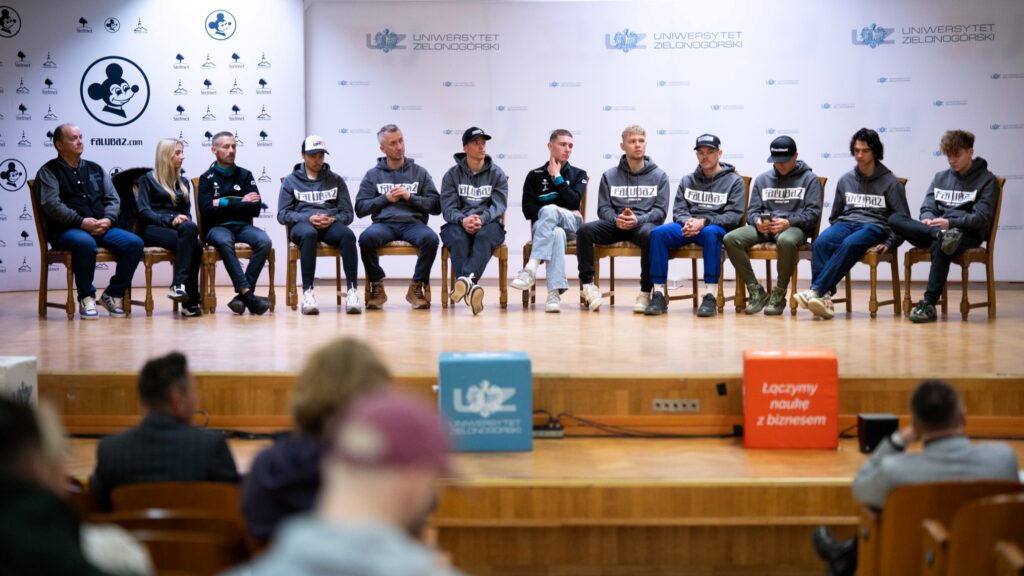 Kilkanaście osób siedzących na krzesłach na scenie