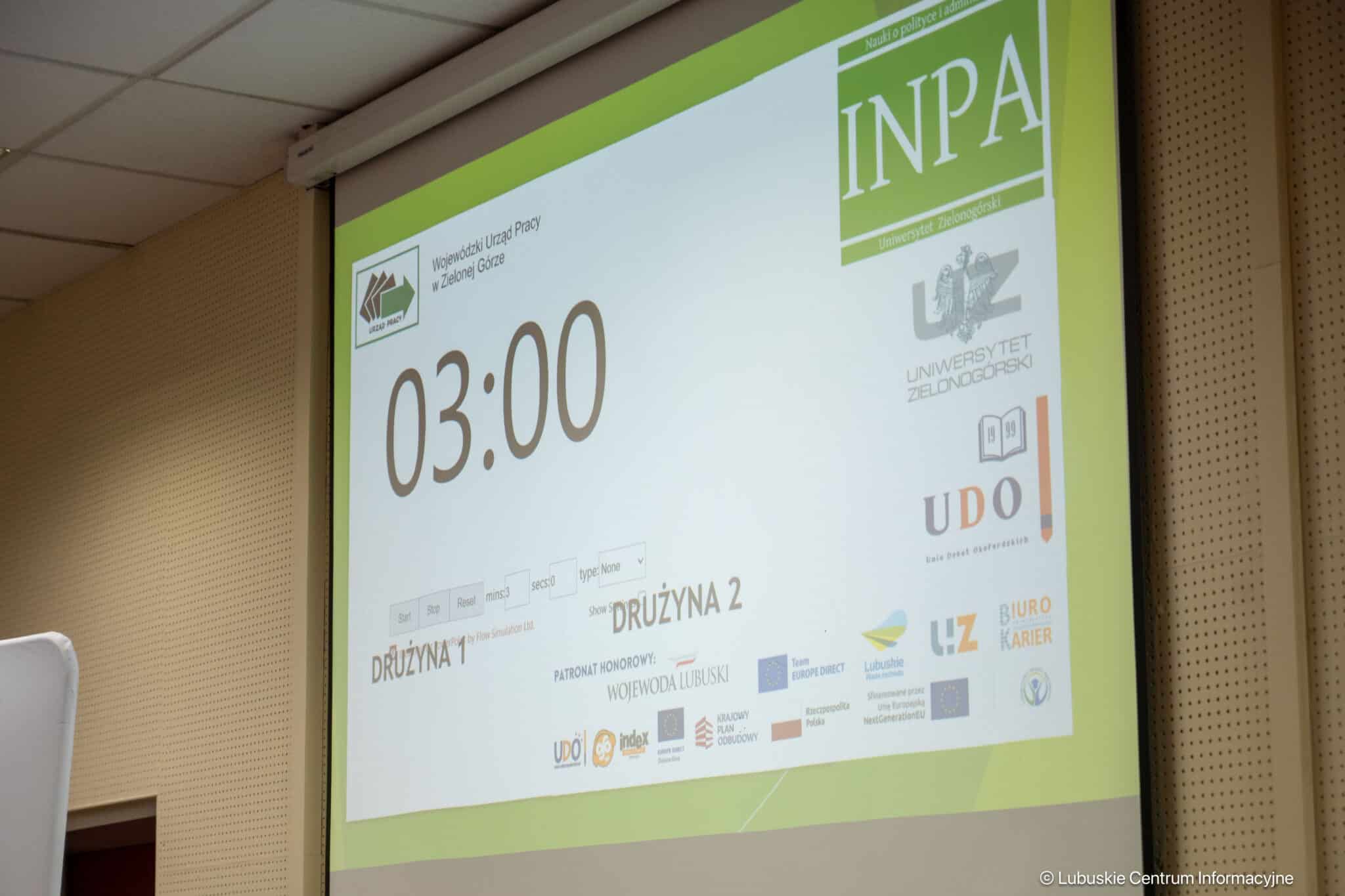 Projection screen showing a large 03:00 countdown with logos and a lime-green border in a conference room.
