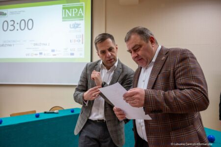Two men in business suits lean over a document during a presentation in a conference room.
