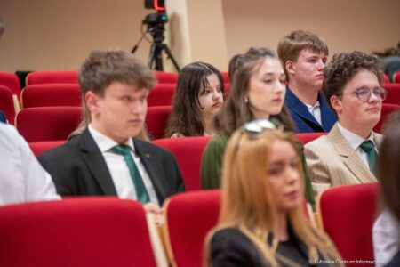 Group of young adults seated in red theater chairs at a conference, listening attentively.