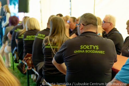 Group of people wearing matching black shirts with lime text, attending a formal event or meeting outdoors/under a tent.
