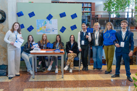 Group of students at an EU information booth in a library, holding small EU flags and brochures.