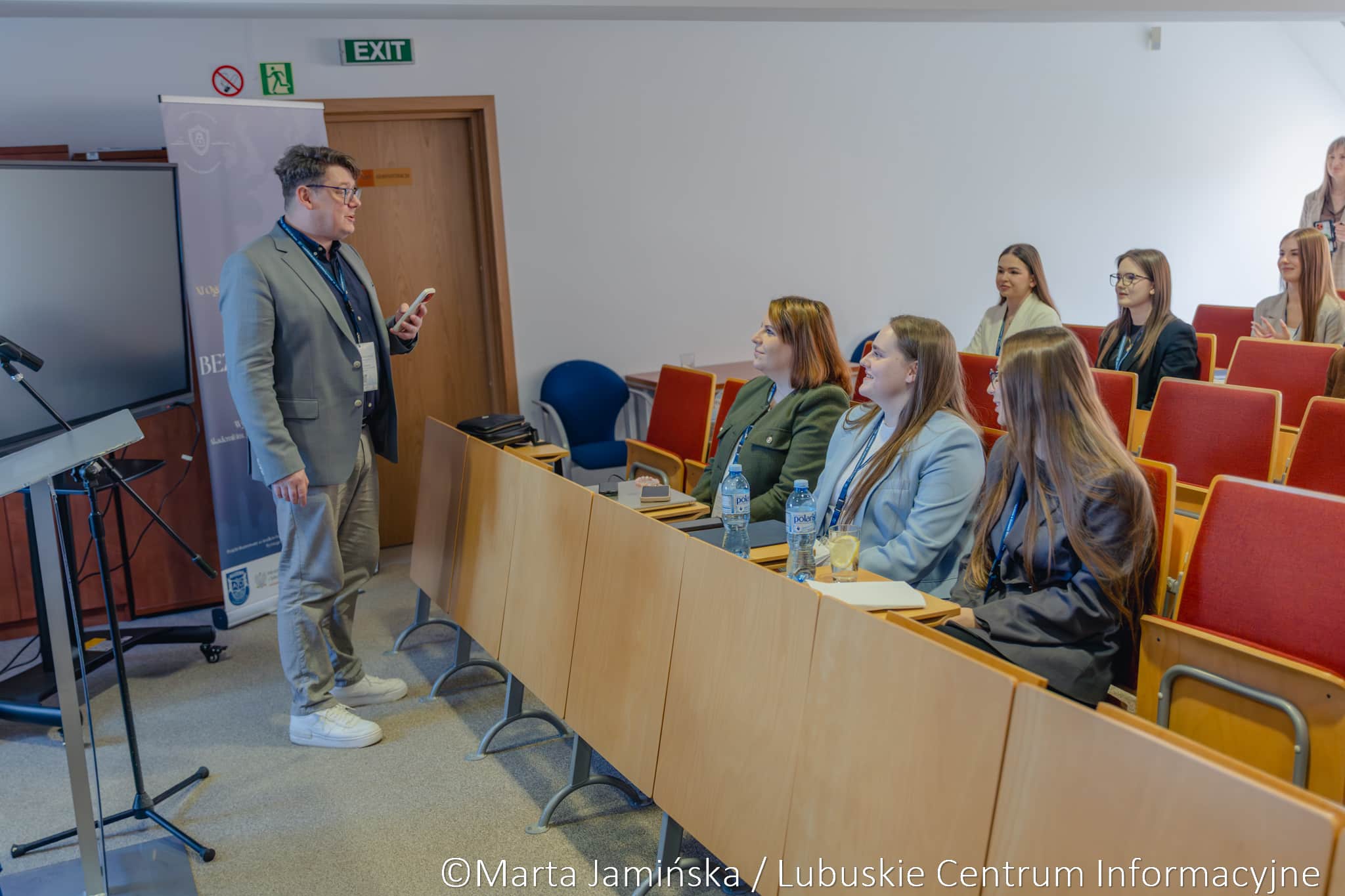Male presenter in a gray suit speaks to a small classroom audience of young women in a lecture hall