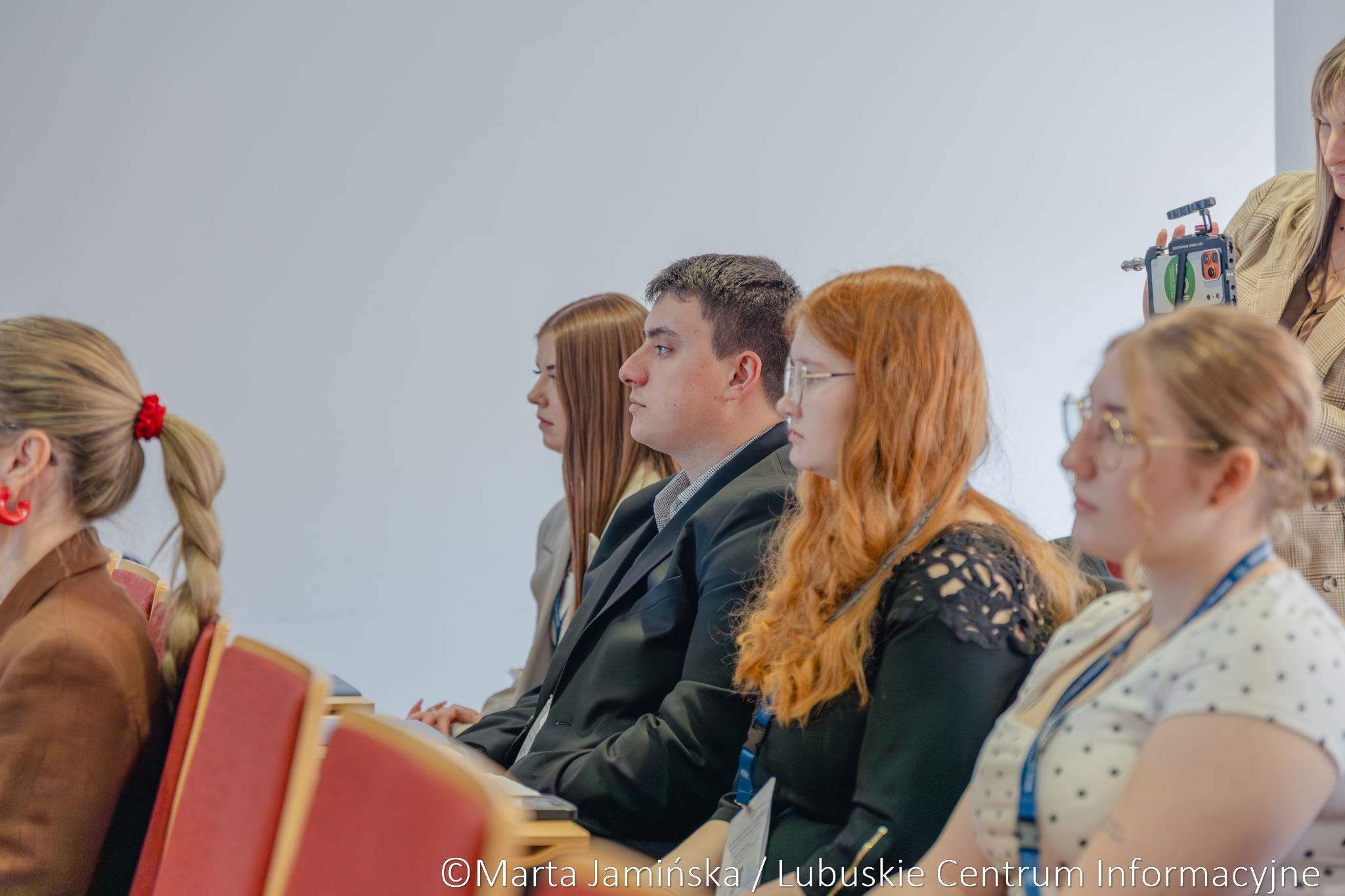 Group of young adults seated in a conference room, listening attentively.